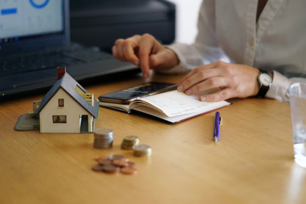 woman focused on her laptop, with a house model displayed on the table beside her