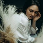 Serene portrait of a woman looking down, surrounded by pampas grass, in a studio setting.