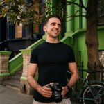 A cheerful photographer holding a camera, captured on a colorful London street.